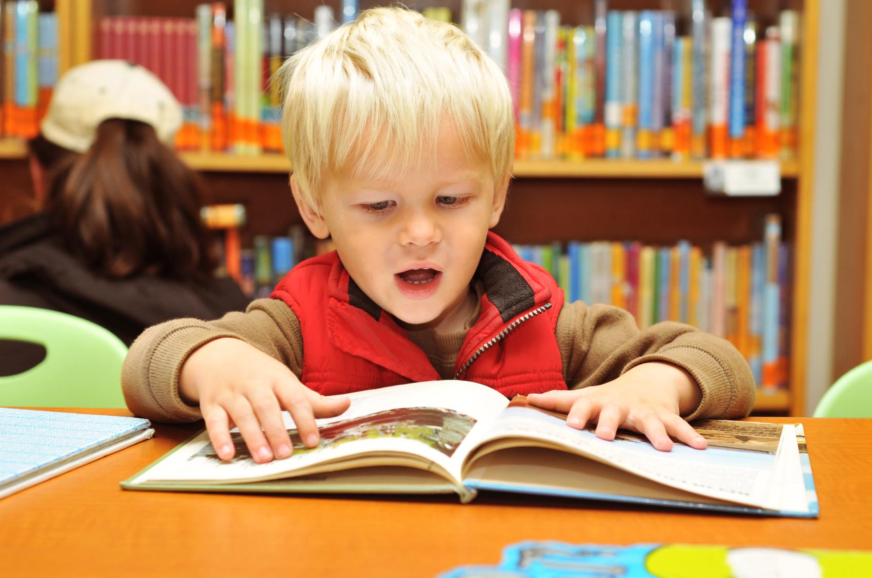 four year old boy reading in a library